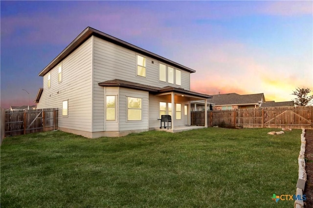 back house at dusk with a lawn and a patio