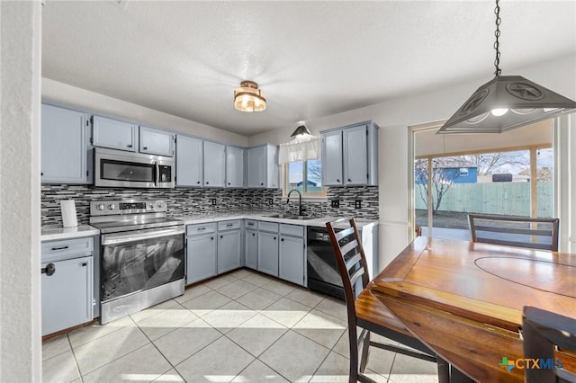 kitchen with appliances with stainless steel finishes, sink, decorative backsplash, hanging light fixtures, and light tile patterned floors