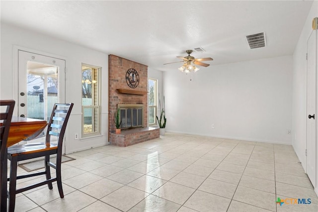 unfurnished living room with ceiling fan, a brick fireplace, and light tile patterned floors