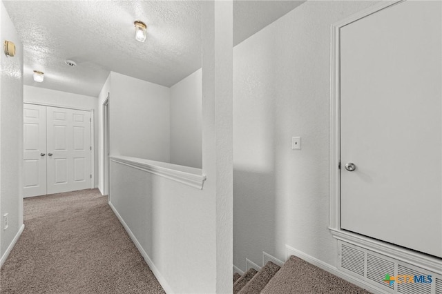 corridor featuring light carpet and a textured ceiling