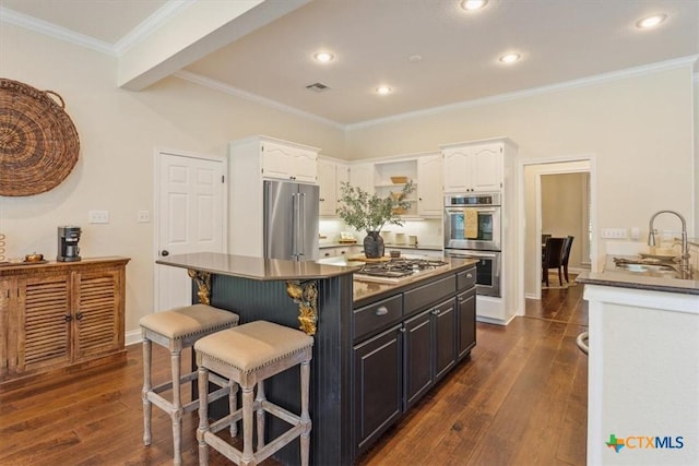 11421 Somerville Dr, Temple, TX 76502 - kitchen featuring appliances with stainless steel finishes, white cabinets, a kitchen breakfast bar, dark wood-style flooring, and ornamental molding
