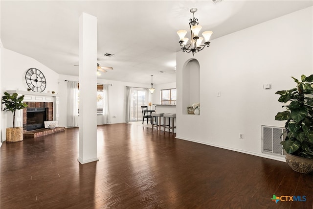 unfurnished living room with ceiling fan with notable chandelier, dark hardwood / wood-style flooring, and a brick fireplace