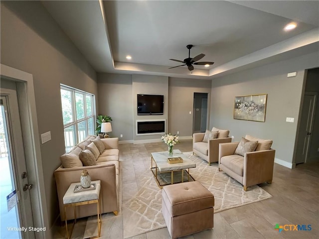 living room featuring baseboards, a raised ceiling, ceiling fan, a fireplace, and recessed lighting