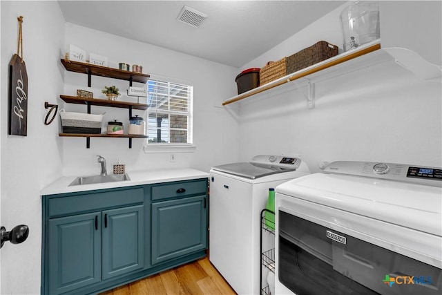 laundry room with visible vents, a sink, separate washer and dryer, cabinet space, and light wood-style flooring