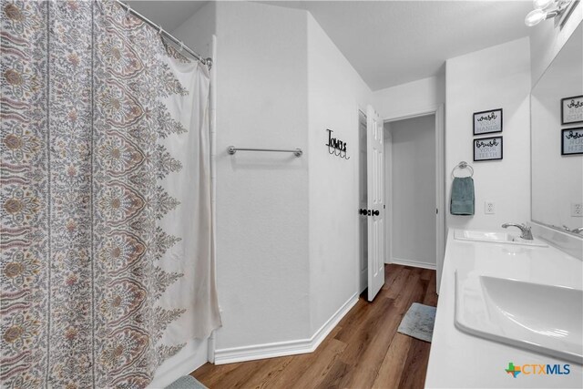 full bath featuring baseboards, wood finished floors, a sink, and double vanity