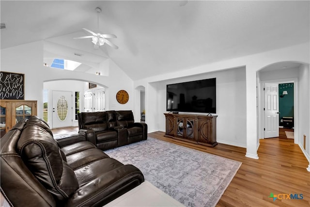 living area with wood finished floors, a ceiling fan, arched walkways, baseboards, and high vaulted ceiling