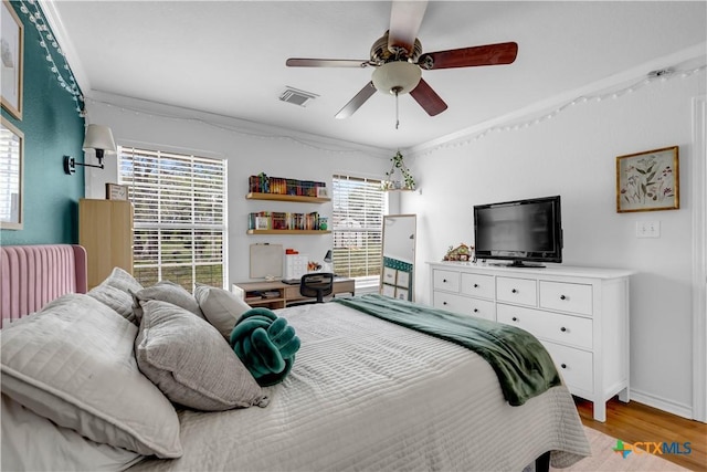 bedroom with a ceiling fan, light wood-type flooring, baseboards, ornamental molding, and visible vents