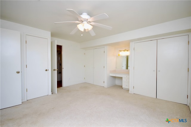 unfurnished bedroom with light carpet, built in desk, ceiling fan, and ensuite bathroom