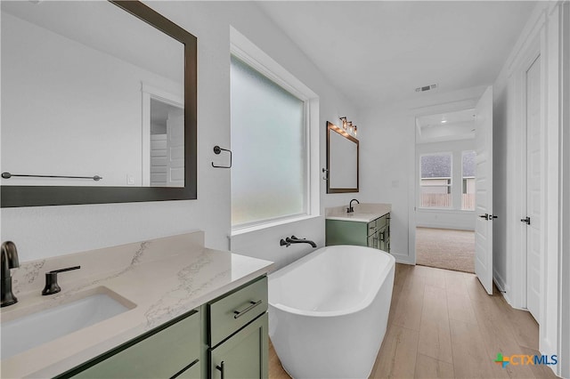 4146 Turning Leaf Dr, Nolanville, TX 76559 - bathroom featuring visible vents, a freestanding tub, wood finished floors, two vanities, and a sink