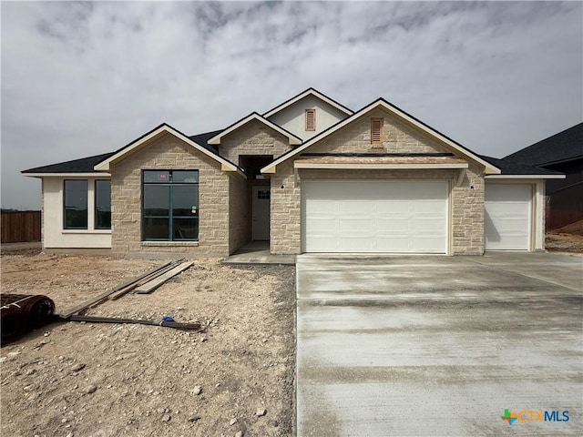 view of front of home with stone siding, an attached garage, and driveway