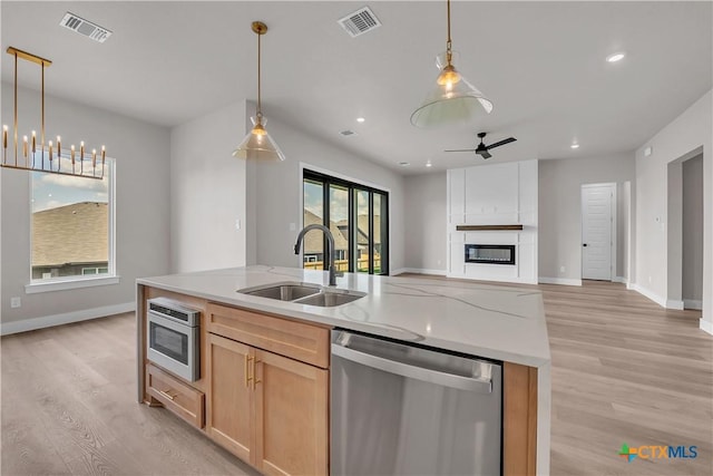 kitchen featuring sink, decorative light fixtures, light brown cabinets, stainless steel appliances, and a kitchen island with sink