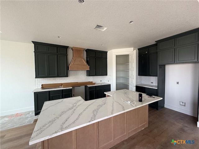 kitchen featuring a spacious island, light stone counters, custom exhaust hood, and tasteful backsplash