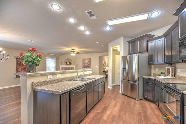 kitchen featuring visible vents, light wood-style flooring, an island with sink, a sink, and black appliances