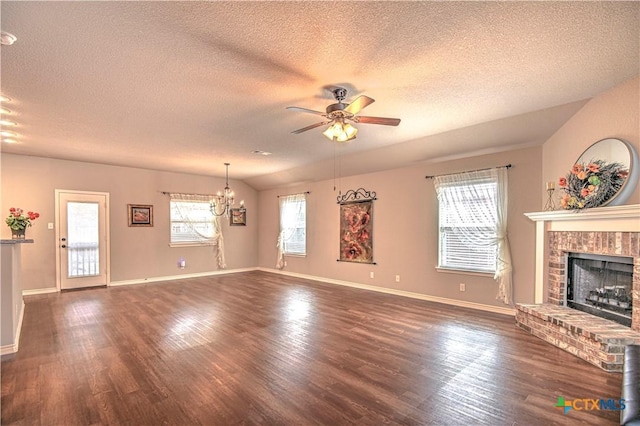 unfurnished living room with dark wood-type flooring, ceiling fan with notable chandelier, a textured ceiling, baseboards, and a brick fireplace