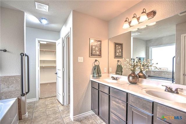 full bath featuring a textured ceiling, double vanity, visible vents, and a sink