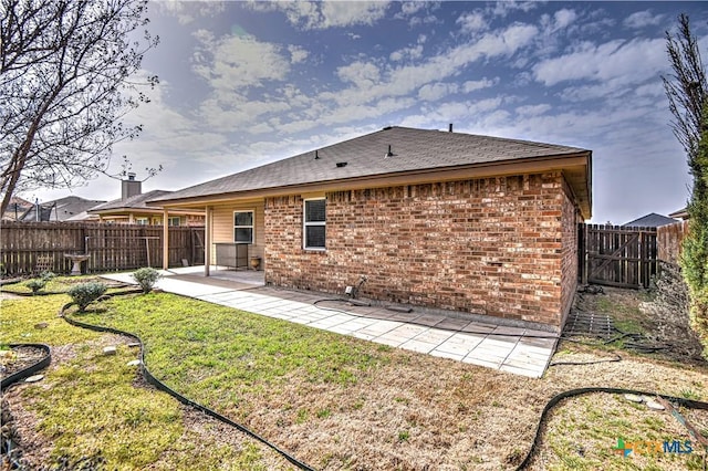 back of house with brick siding, a fenced backyard, a lawn, and a patio