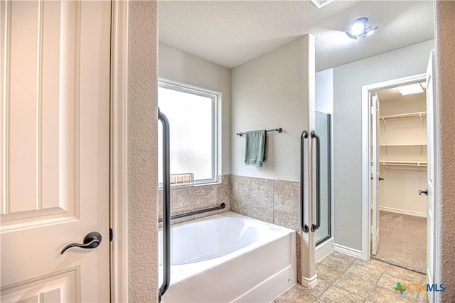 full bath featuring a bath, a spacious closet, a stall shower, and a textured ceiling