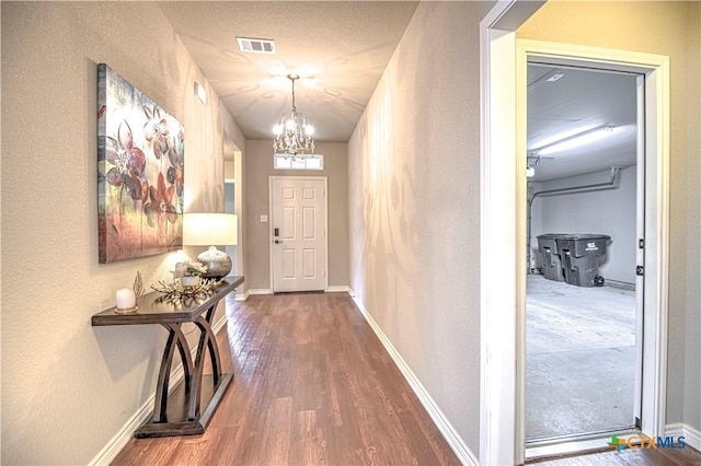 doorway with visible vents, an inviting chandelier, baseboards, and wood finished floors