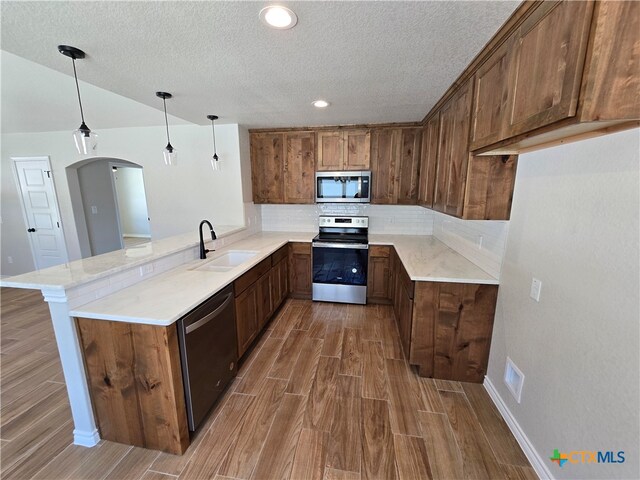 kitchen featuring appliances with stainless steel finishes, hanging light fixtures, hardwood / wood-style floors, sink, and kitchen peninsula