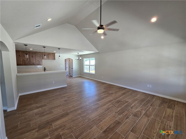 unfurnished living room with high vaulted ceiling, dark hardwood / wood-style floors, and ceiling fan with notable chandelier