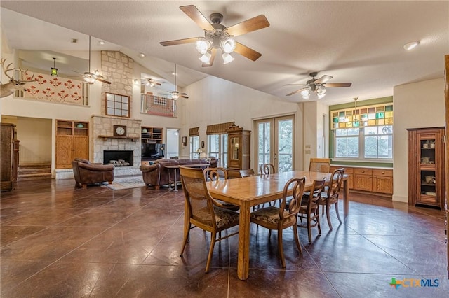 dining area featuring french doors, a stone fireplace, high vaulted ceiling, a textured ceiling, and dark tile patterned flooring