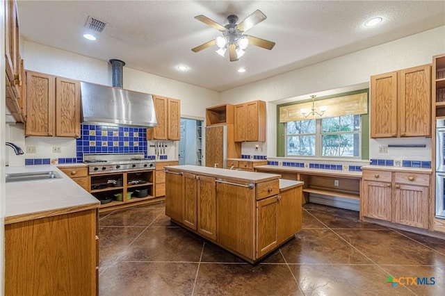 kitchen featuring wall chimney exhaust hood, sink, a kitchen island, stainless steel gas stovetop, and decorative backsplash