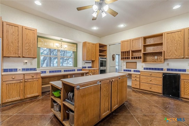 kitchen featuring a kitchen island, ceiling fan with notable chandelier, pendant lighting, dark tile patterned flooring, and stainless steel double oven