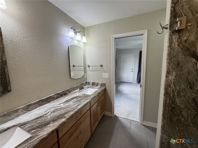 bathroom with a textured wall, baseboards, and vanity