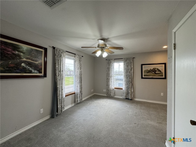 spare room featuring carpet floors, ceiling fan, visible vents, and a wealth of natural light