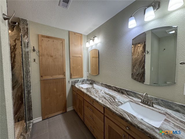full bath with a sink, a textured ceiling, double vanity, and visible vents