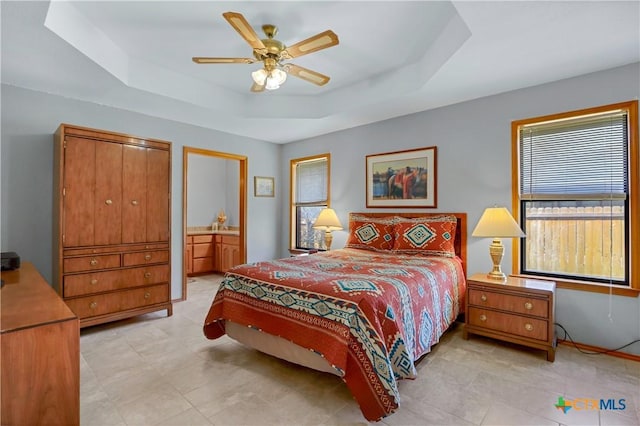 bedroom with a raised ceiling, ensuite bathroom, and ceiling fan