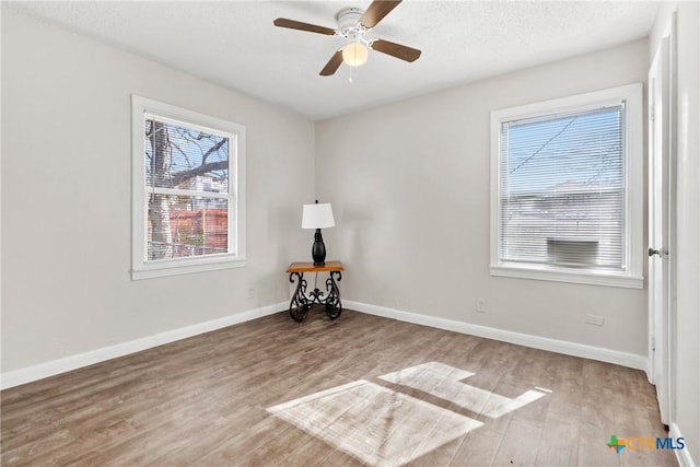 interior space with ceiling fan, a textured ceiling, baseboards, and wood finished floors