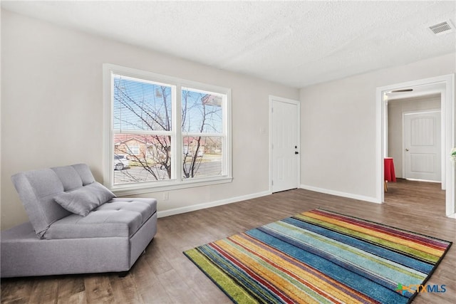 living area featuring a textured ceiling, wood finished floors, visible vents, and baseboards