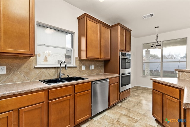 kitchen with decorative backsplash, appliances with stainless steel finishes, sink, an inviting chandelier, and hanging light fixtures