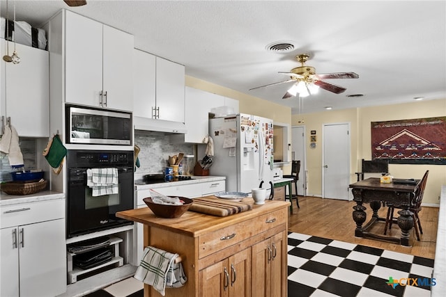 kitchen featuring white cabinets, light wood-type flooring, black appliances, and tasteful backsplash