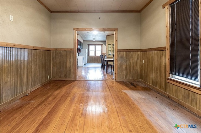 spare room with ornamental molding, wooden walls, and light wood-type flooring