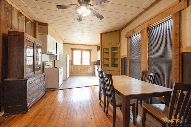 dining room featuring wooden walls, ornamental molding, ceiling fan, and light wood-type flooring