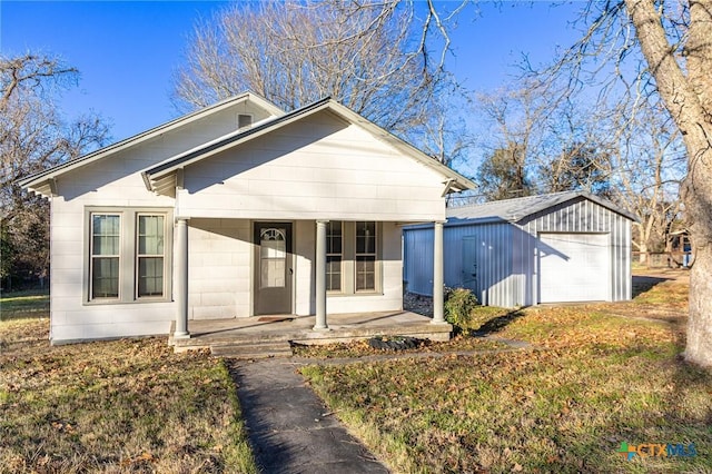 bungalow with a porch, a garage, an outdoor structure, and a front lawn