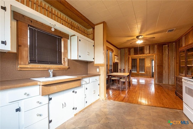 kitchen featuring sink, ceiling fan, wooden walls, white range with electric stovetop, and white cabinets