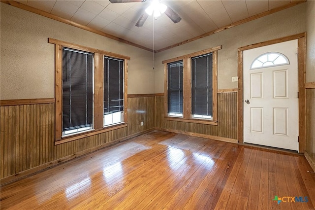 entrance foyer featuring hardwood / wood-style flooring, ceiling fan, ornamental molding, and wood walls