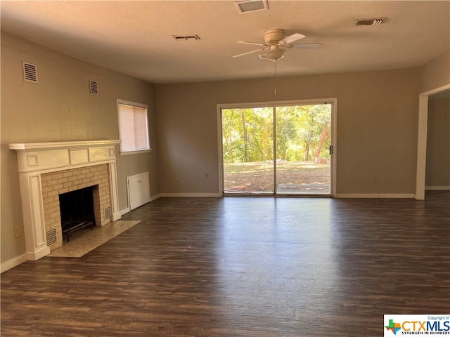 unfurnished living room with a brick fireplace, dark hardwood / wood-style flooring, a textured ceiling, and ceiling fan