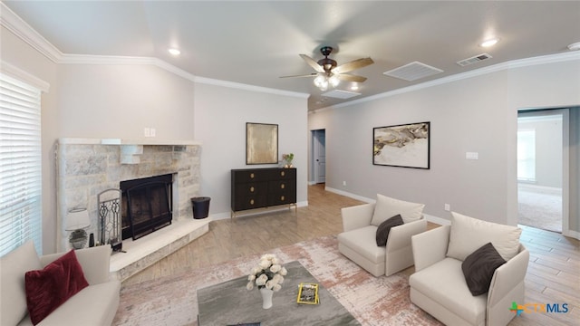 living room with crown molding, a stone fireplace, ceiling fan, and light hardwood / wood-style flooring