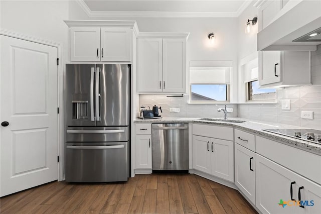 kitchen with a sink, white cabinetry, appliances with stainless steel finishes, wall chimney range hood, and crown molding