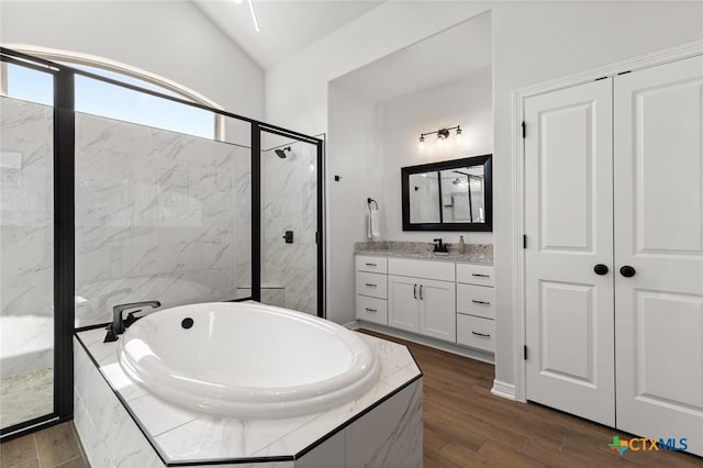 bathroom with wood finished floors, vanity, vaulted ceiling, a marble finish shower, and a bath