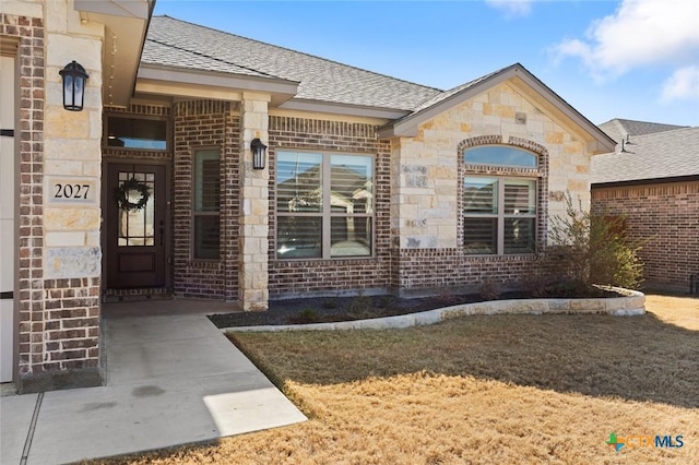 doorway to property with a shingled roof, stone siding, and brick siding