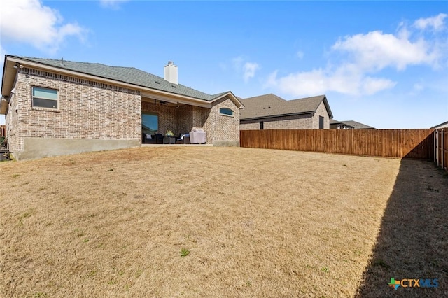 back of property with a chimney, brick siding, a yard, and a fenced backyard