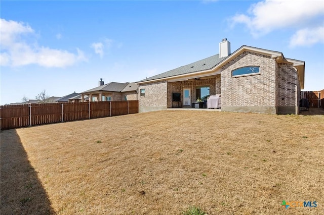 back of house with a patio, a chimney, fence, a yard, and brick siding