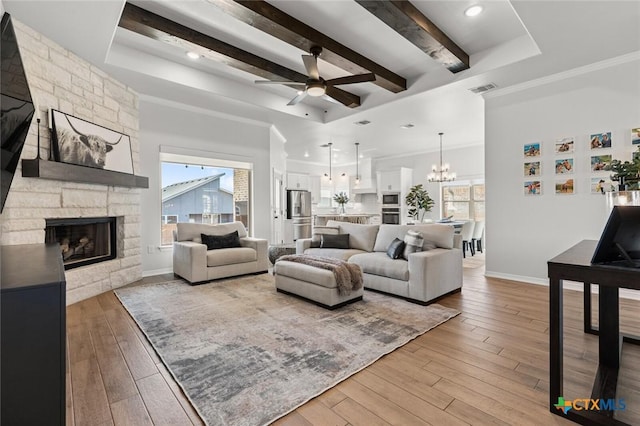 living room featuring light wood-style floors, a fireplace, visible vents, and beamed ceiling