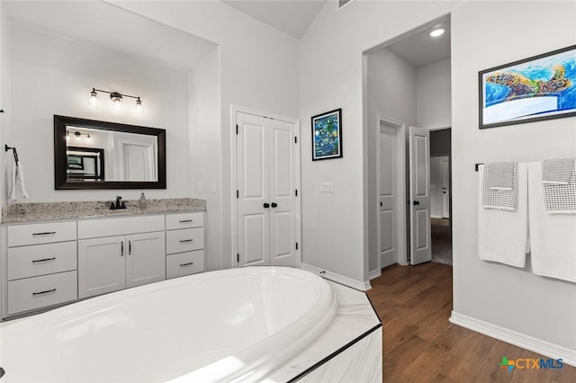 bathroom featuring vanity, wood finished floors, a bathing tub, and baseboards