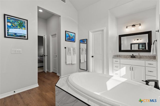 bathroom featuring a garden tub, vanity, baseboards, and wood finished floors